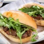 Savory beef sandwiches topped with fresh arugula served in soft bread.