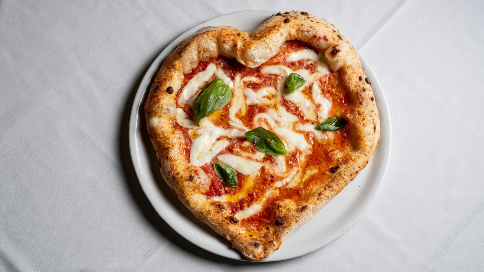 Delicious heart-shaped pizza topped with fresh basil and mozzarella on a white plate.