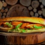 Close-up of a crispy chicken sandwich with fresh lettuce on a wooden board, perfect for a tasty meal.